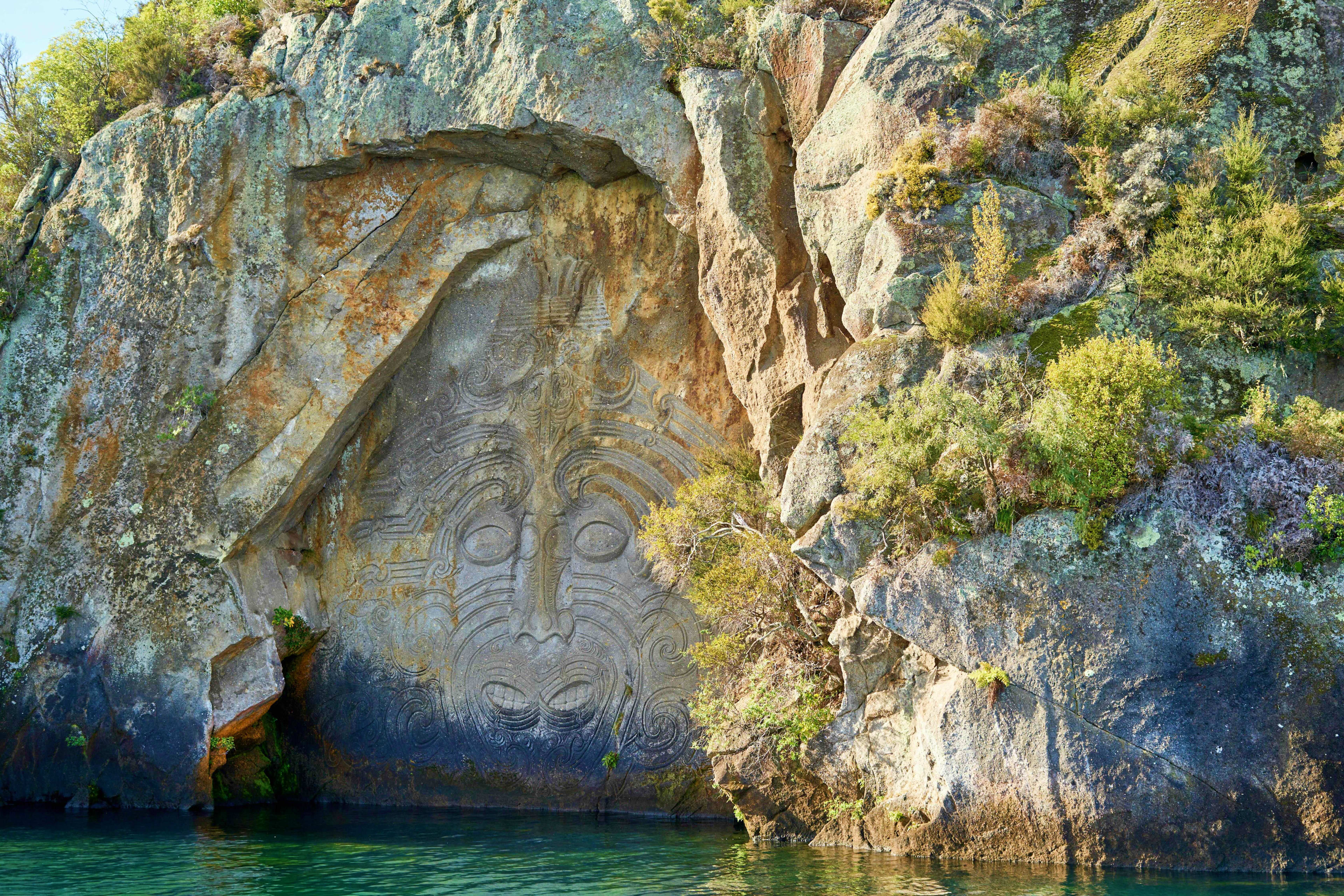 New Zealand Ancient Maori rock carving (pataka) on cliff face above turquoise water, Toutai New Zealand